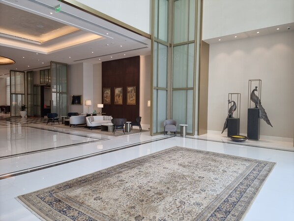 A spacious lobby with a large, ornate rug, seating areas, and artwork on the walls.