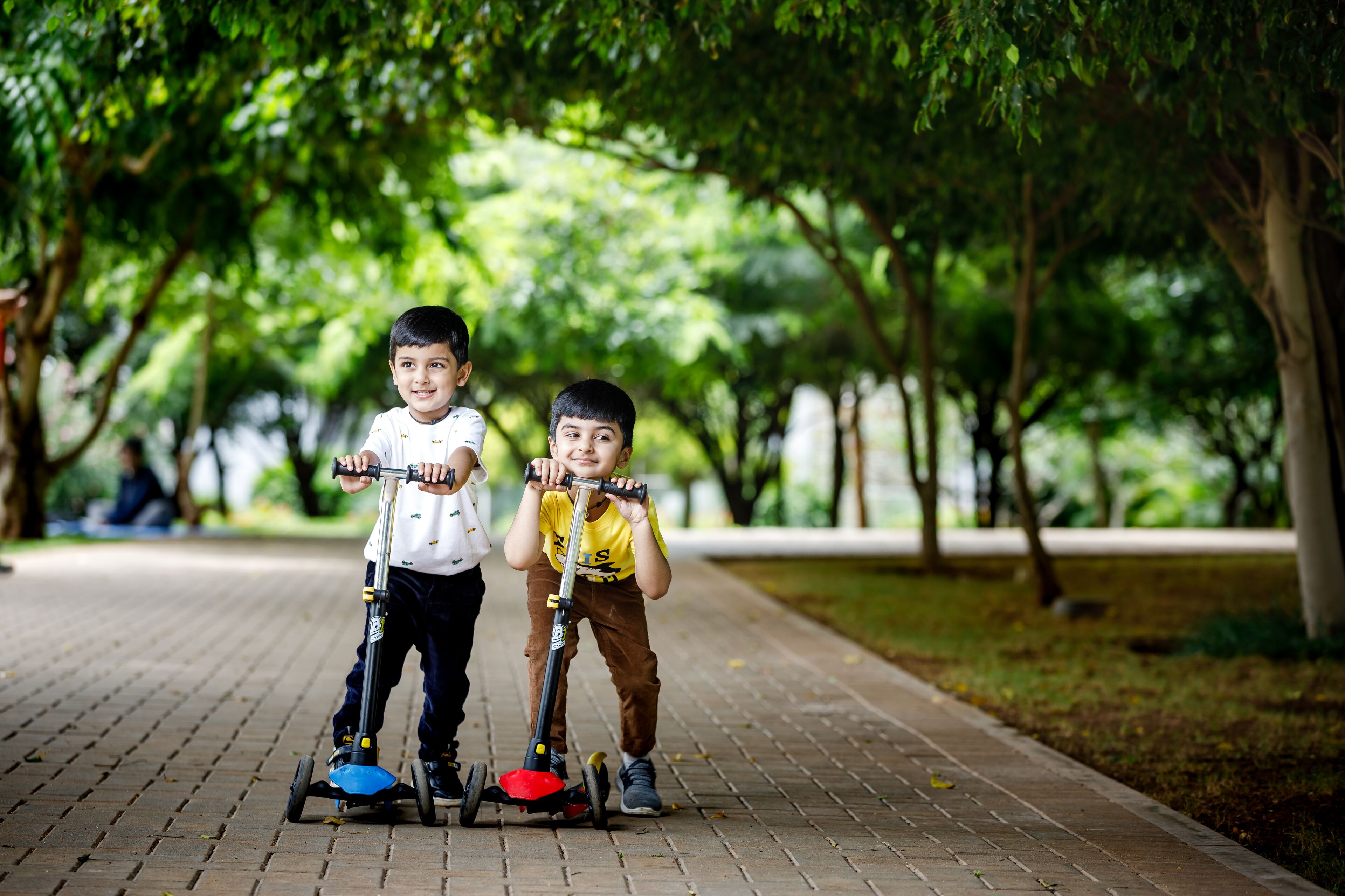 Deux enfants font de la trottinette sur un chemin aménagé dans un parc.
