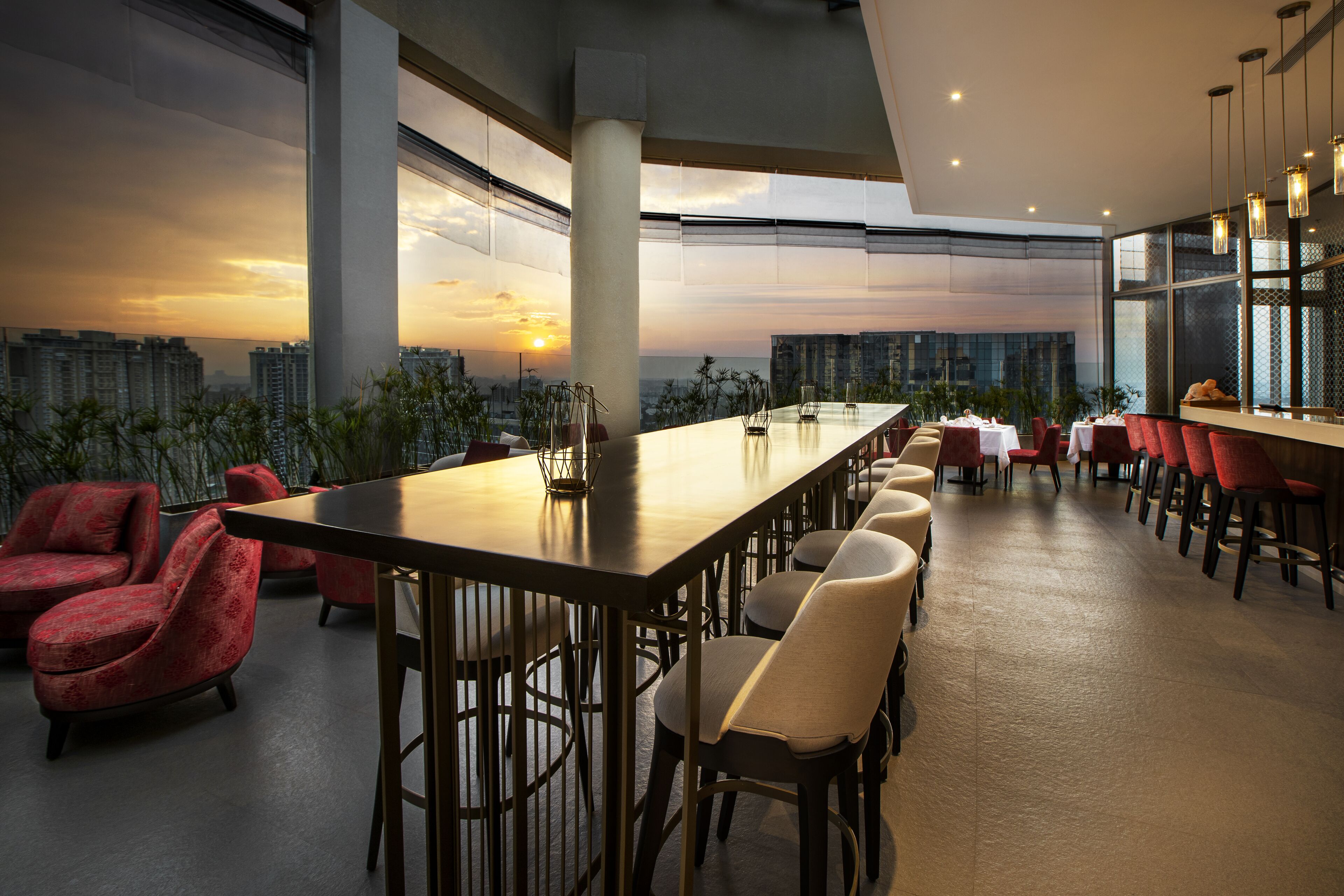 A modern dining area with a long table, red and beige chairs, and large windows offering a city view.