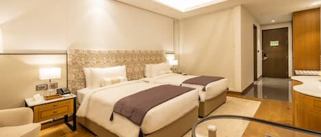 A hotel room with two beds, a desk, a chair, a round table, and a bathroom.