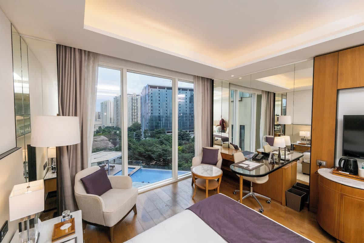 Habitación de hotel con cama, dos sillones, escritorio, televisor y un amplio ventanal con vistas a la ciudad.