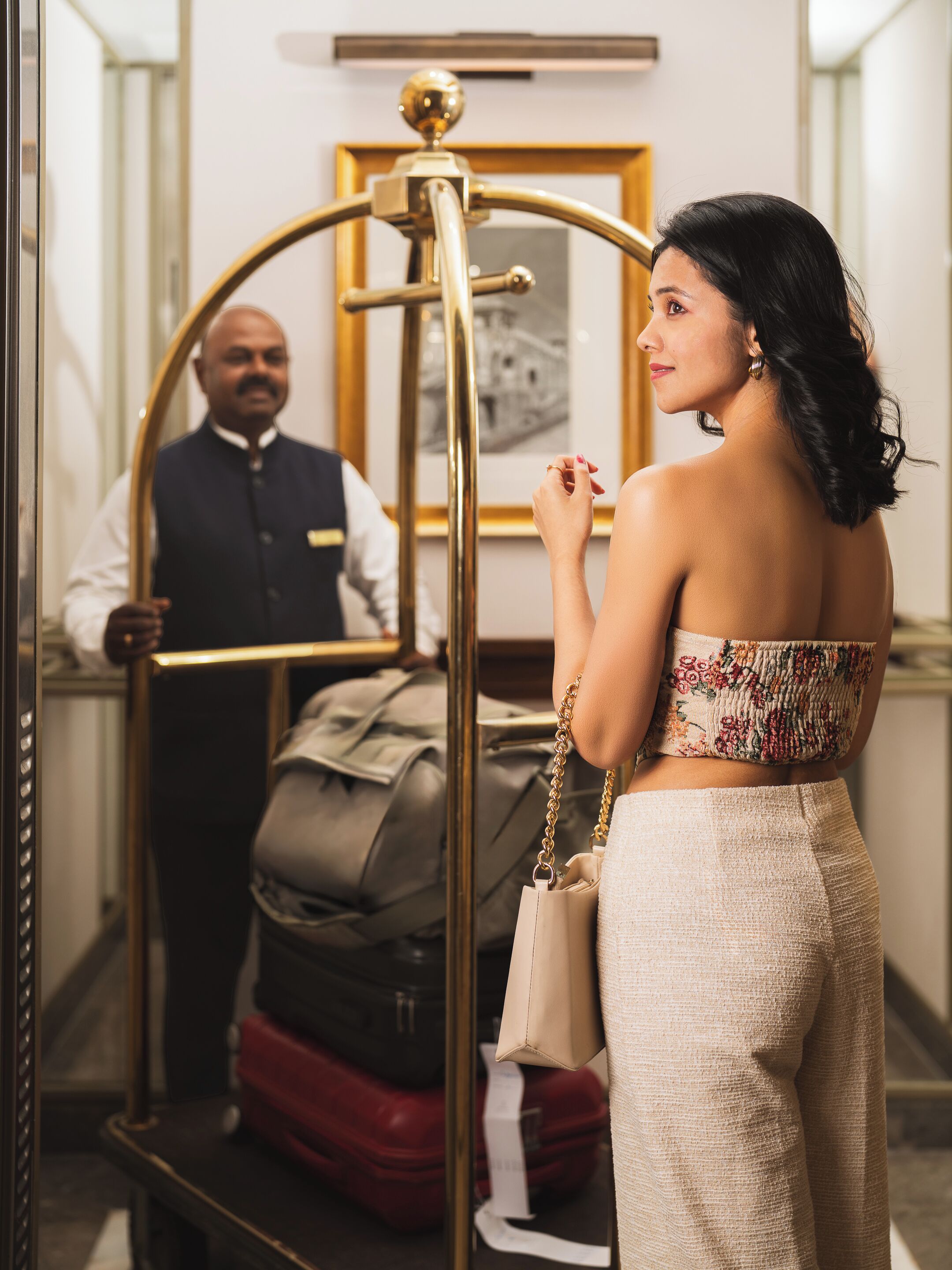 A woman standing next to a luggage cart in a hotel lobby with a framed picture on the wall.