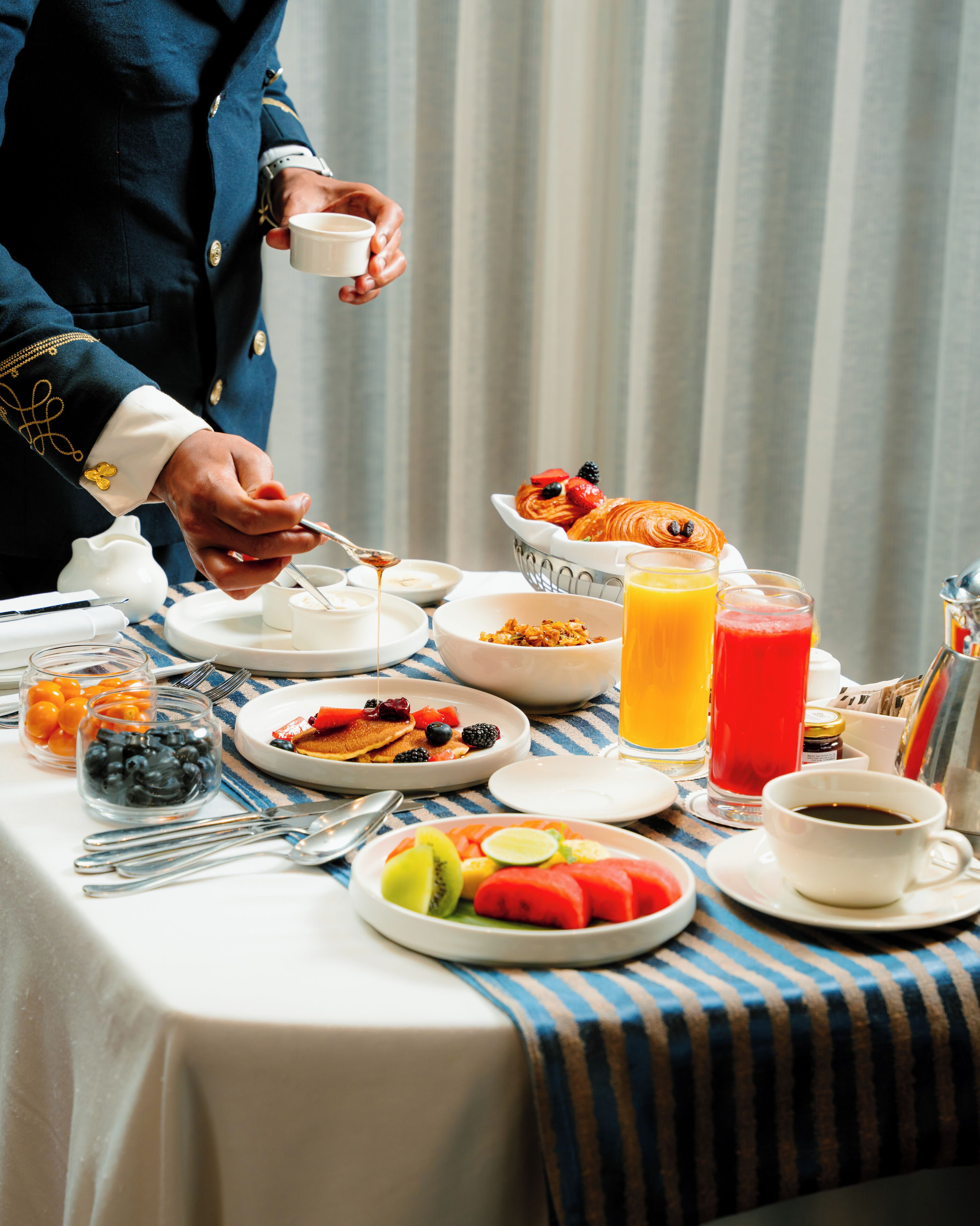 A breakfast setting with a variety of food items, including fruits, pastries, and beverages, arranged on a table.