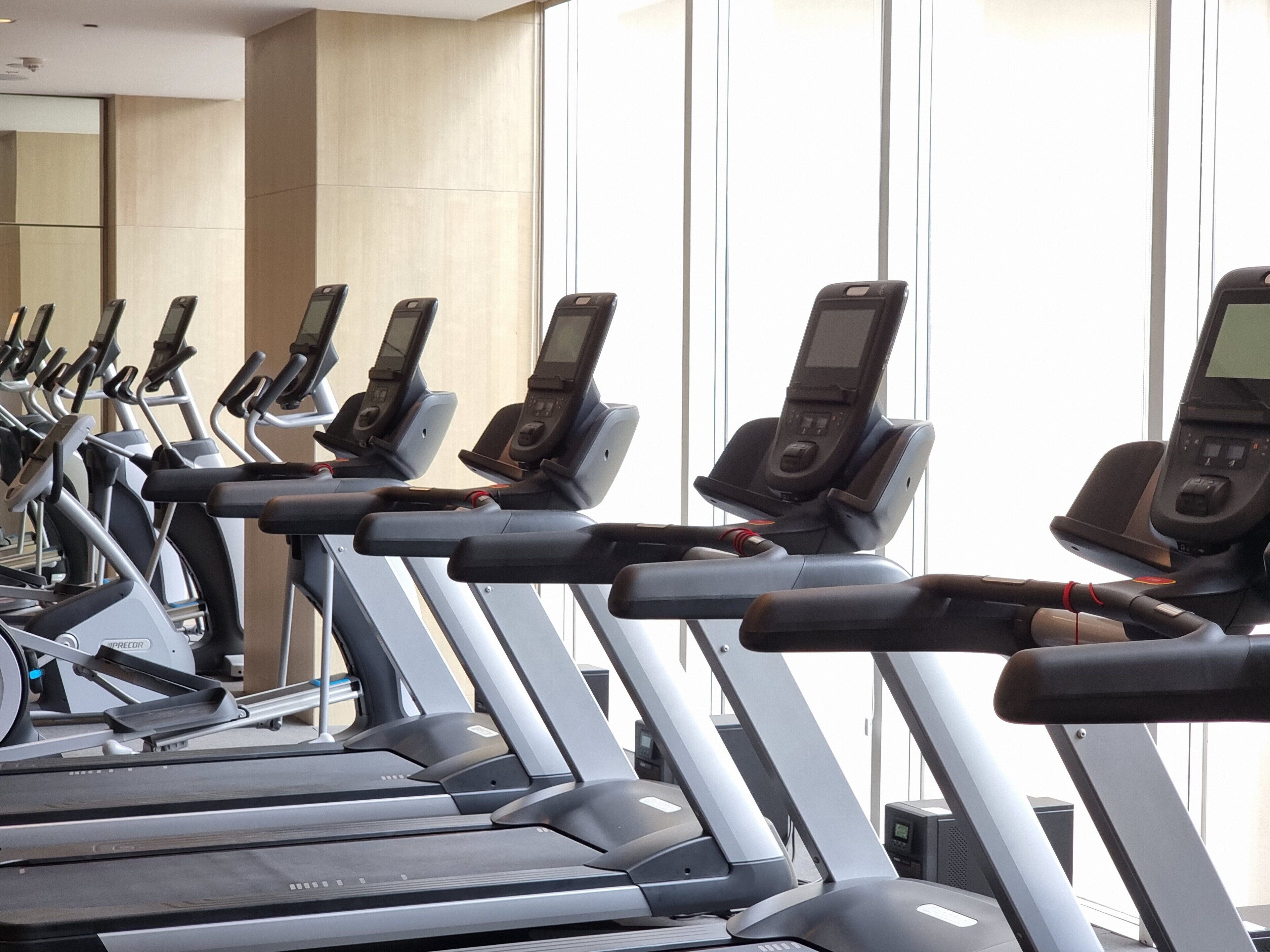 A row of stationary bikes in a gym with a large window in the background.