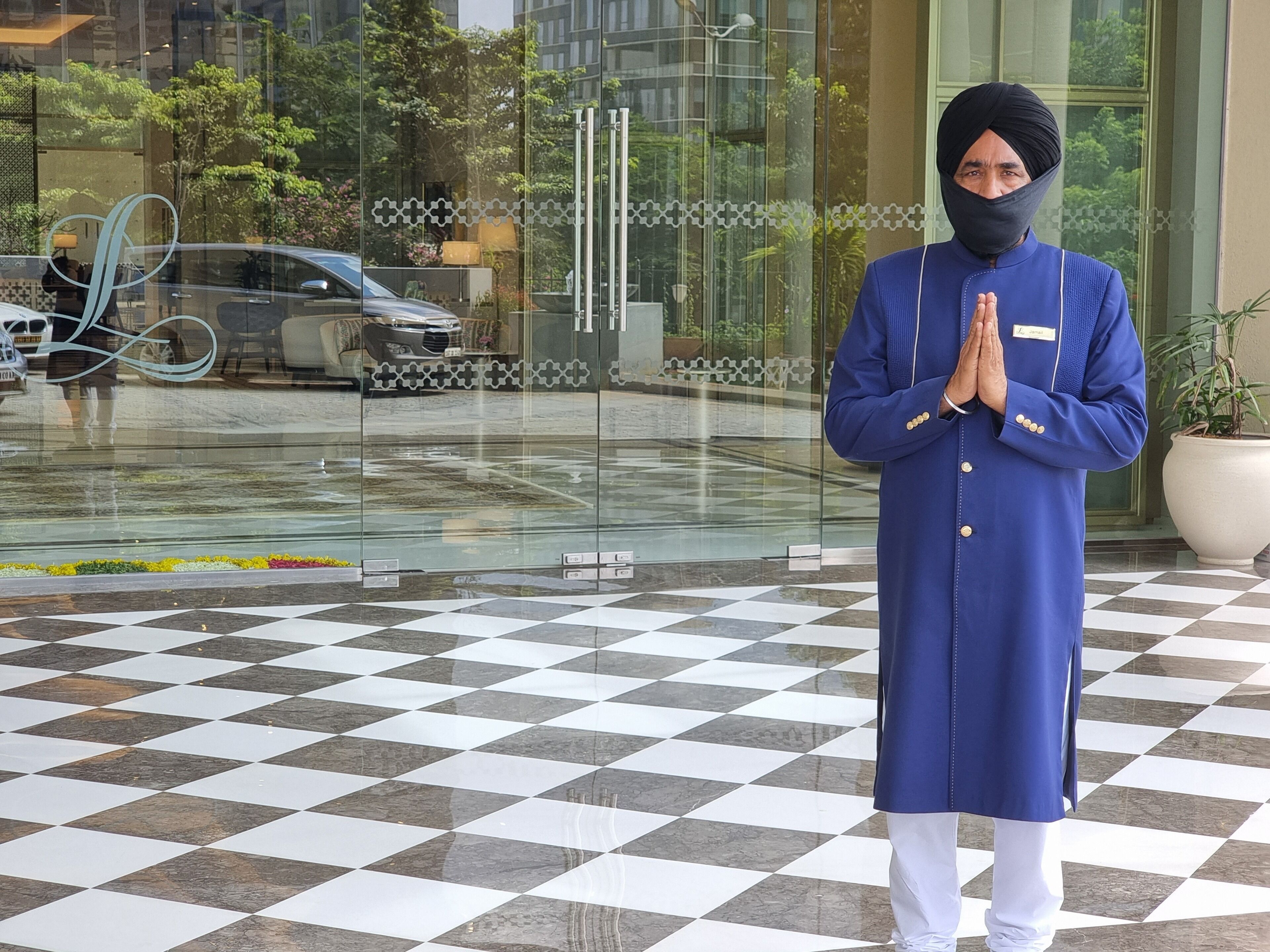 A person in traditional attire standing in front of a building with a checkered floor and glass entrance.