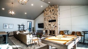 Una sala de estar moderna con mesa de billar, chimenea de piedra y un rincón de estar acogedor.