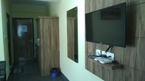 Una habitación con un armario de madera, un televisor montado en la pared y un cubo de basura azul.