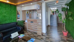 Zona de recepción con mostrador de madera, un sofá de cuero negro y una mesa de centro de vidrio con una computadora portátil y folletos.