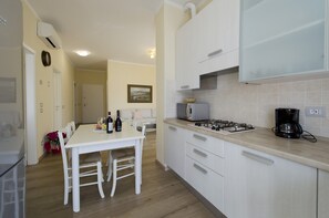 Une cuisine avec des meubles blancs, une cuisinière à gaz, un four à micro-ondes et une machine à café.