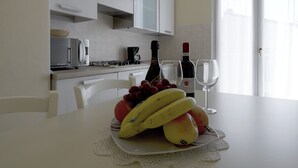 Een keuken met witte kastjes, een magnetron, een koffiezetapparaat en een eettafel met een schaal fruit.