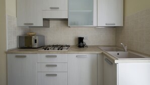 Een keuken met een magnetron, gasfornuis, koffiezetapparaat en een spoelbak.