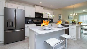 Una cocina moderna con electrodomésticos de acero inoxidable, una isla central con taburetes y flores decorativas.