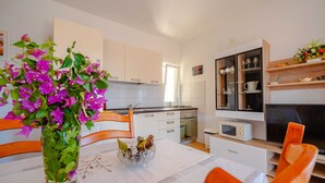 Una cucina moderna con mobili bianchi, un tavolo da pranzo con sedie arancioni e un vaso di fiori viola.