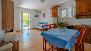 Una cucina con mobili in legno, un tavolo da pranzo con tovaglia blu, un frigorifero e una finestra con persiane.