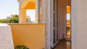 Ingresso di un edificio con porta in vetro, una pianta in vaso e un balcone con ringhiere.