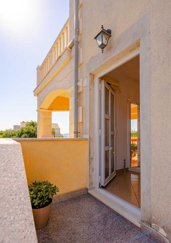 A building entrance with a glass door, a potted plant, and a balcony with railings. - Apartments Mladenka (Orebic)