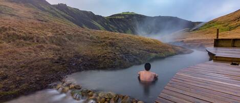 A wooden deck overlooking a hot spring with a person in the water.