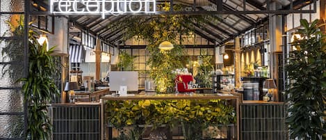 Zona de recepción con letrero de neón, plantas de interior y máquina de café.