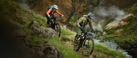 Two mountain bikers on a rocky trail with a stream in the background.