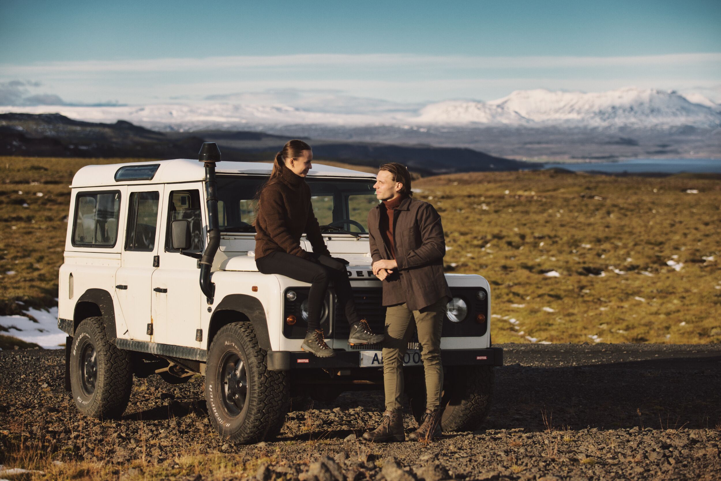 A white SUV parked on a rocky terrain with a mountainous backdrop.