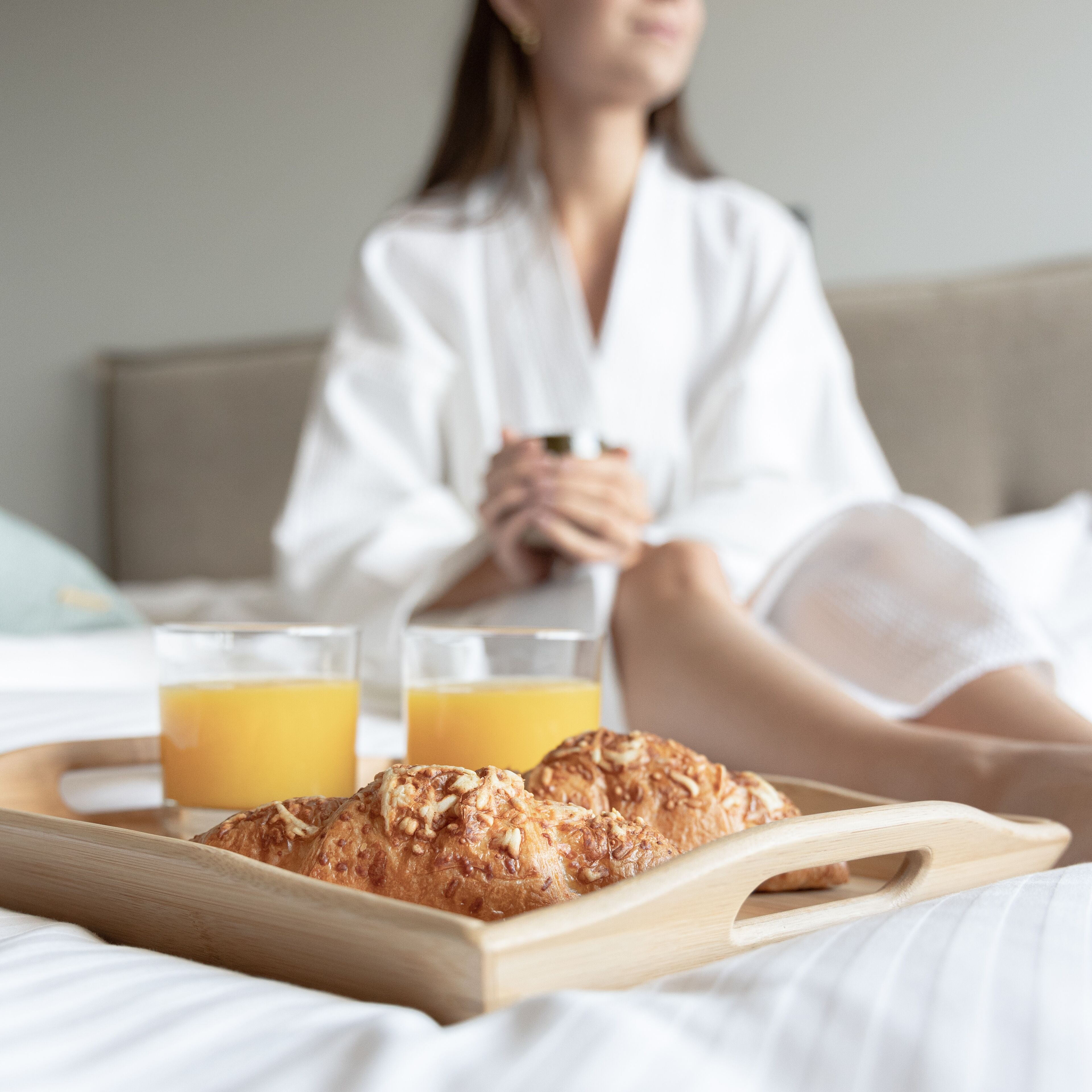 A breakfast tray with croissants and orange juice on a bed.