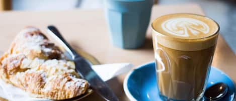 Uma mesa com um doce, uma chávena de café, uma colher e uma chávena azul.