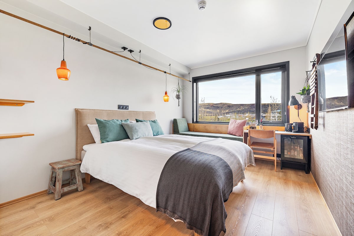 Ein modernes Schlafzimmer mit einem großen Bett, einem Schreibtisch und Blick ins Freie.