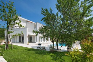 Una moderna casa a due piani con piscina, area salotto esterna e prato curato.