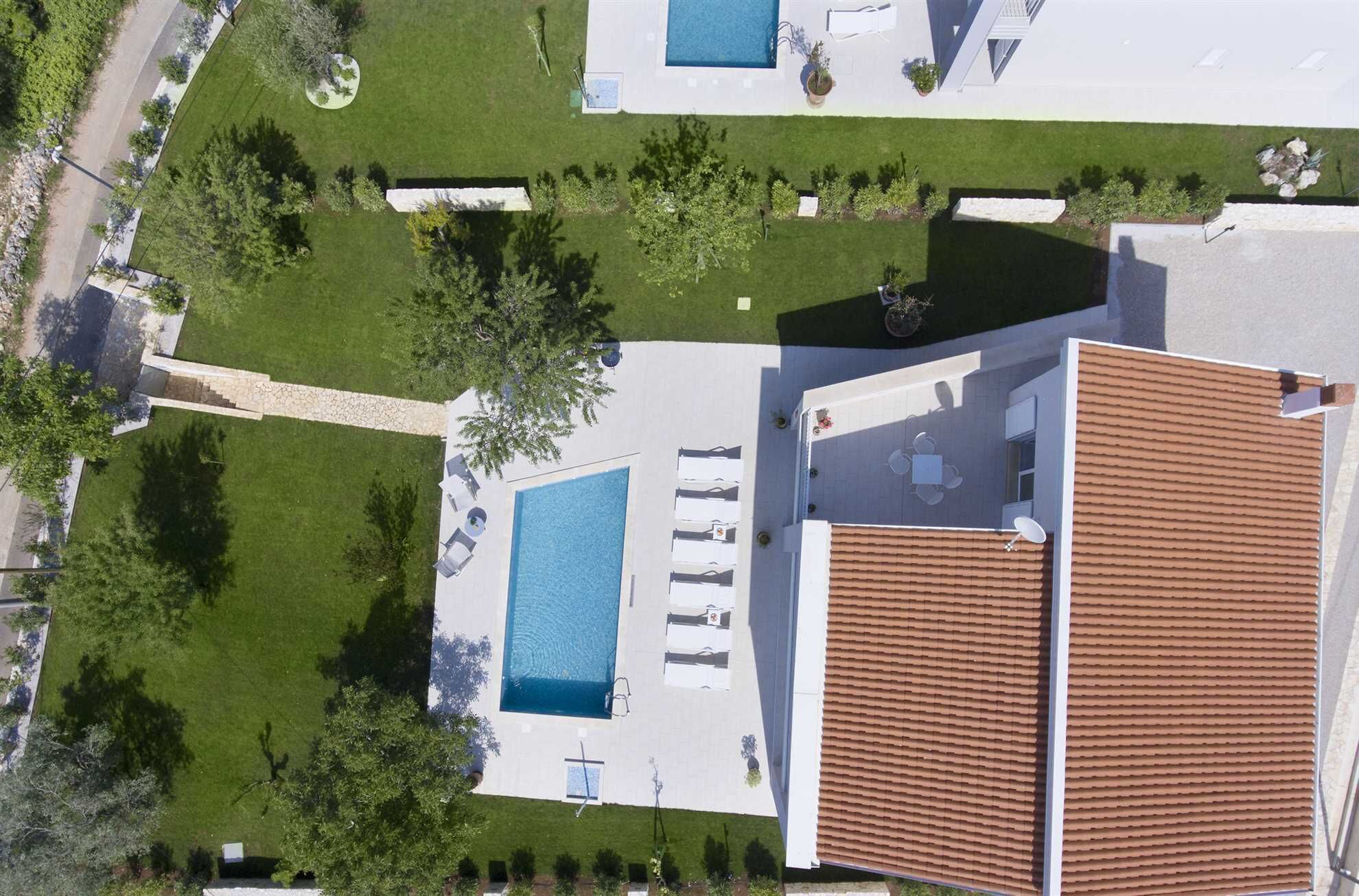 A rooftop pool with sun loungers, a stone pathway, and a tiled roof.