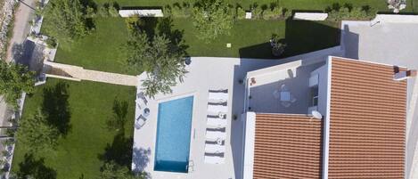 A rooftop pool with sun loungers, a stone pathway, and a tiled roof.