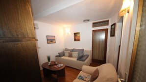 A living room with a sofa, armchair, coffee table, and a door. - Apartment Amazing Summer (Dubrovnik)