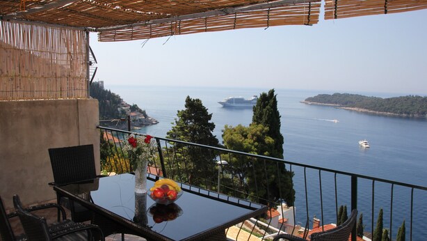 A balcony with a glass table, wicker chairs, and a bowl of fruit. - Apartment Amazing Summer (Dubrovnik)