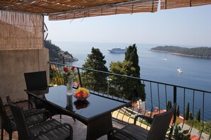 A balcony with a glass table, wicker chairs, and a bowl of fruit. - Apartment Amazing Summer (Dubrovnik)