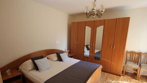 A bedroom with a large bed, wooden wardrobe, and a small chair. - Apartment Amazing Summer (Dubrovnik)