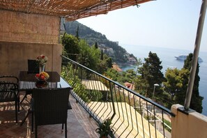 A balcony with a table and chairs, overlooking a coastal landscape with buildings and a ship in the distance. - Apartment Amazing Summer (Dubrovnik)