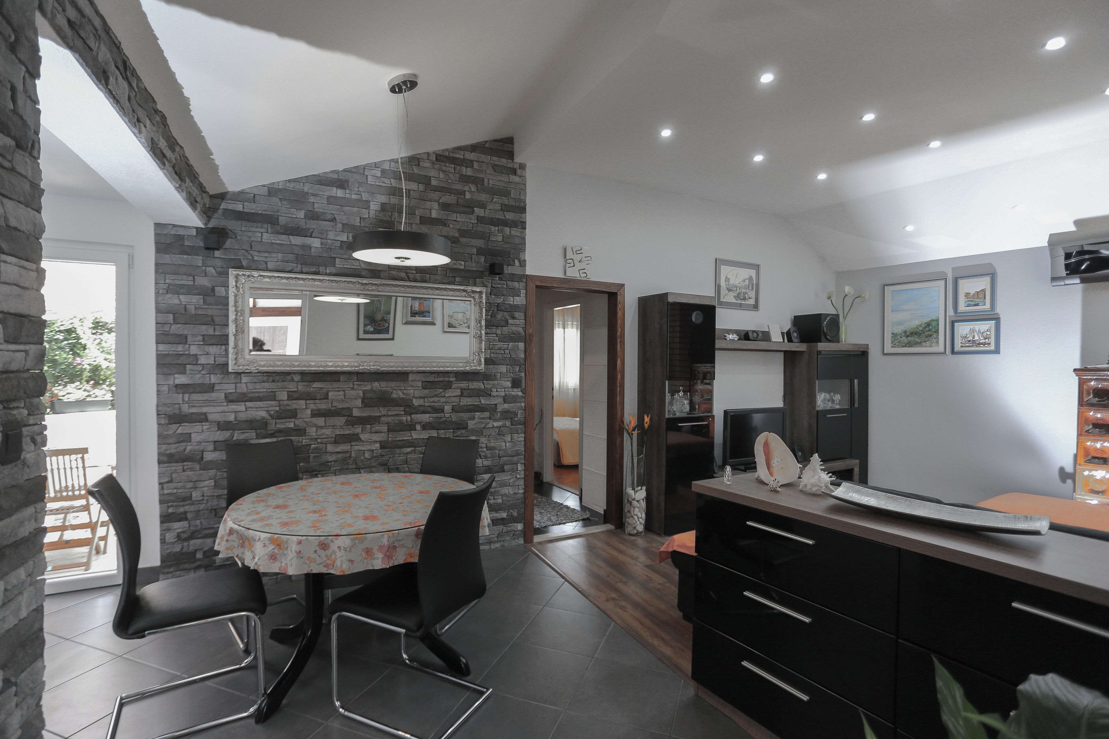 A modern kitchen with a stone wall, a round dining table with chairs, and a large mirror above the table.