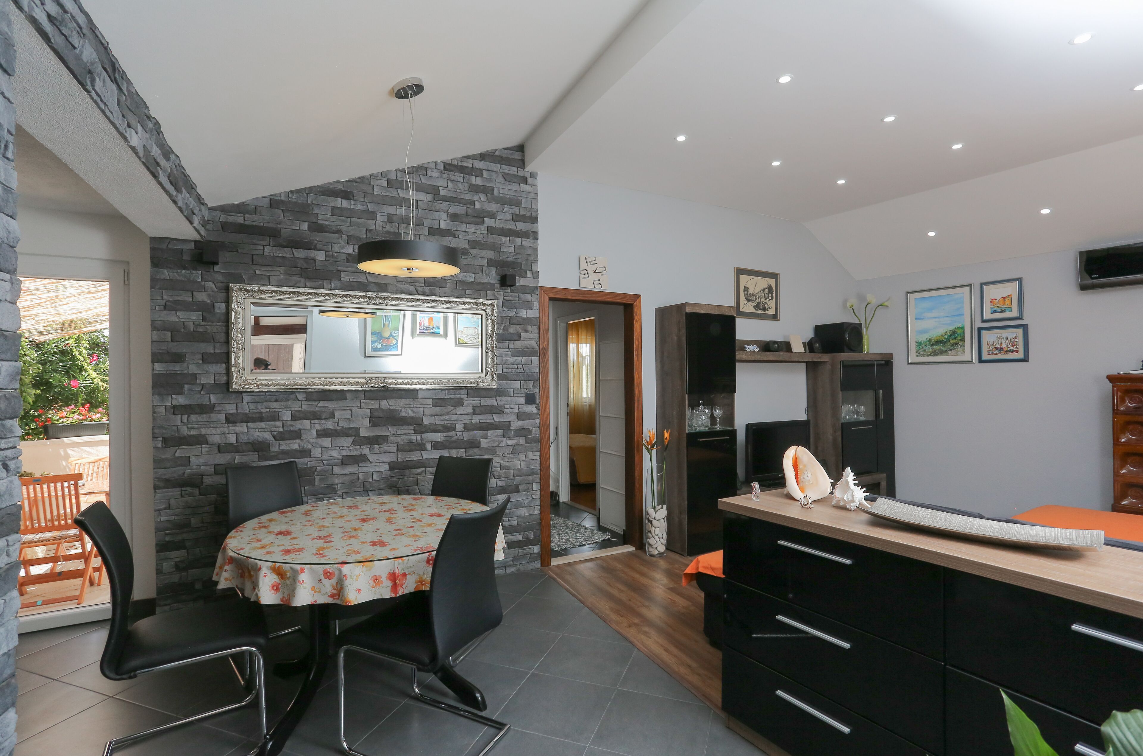 A modern kitchen with a stone accent wall, a dining area with a floral tablecloth, and a wooden cabinet with drawers.
