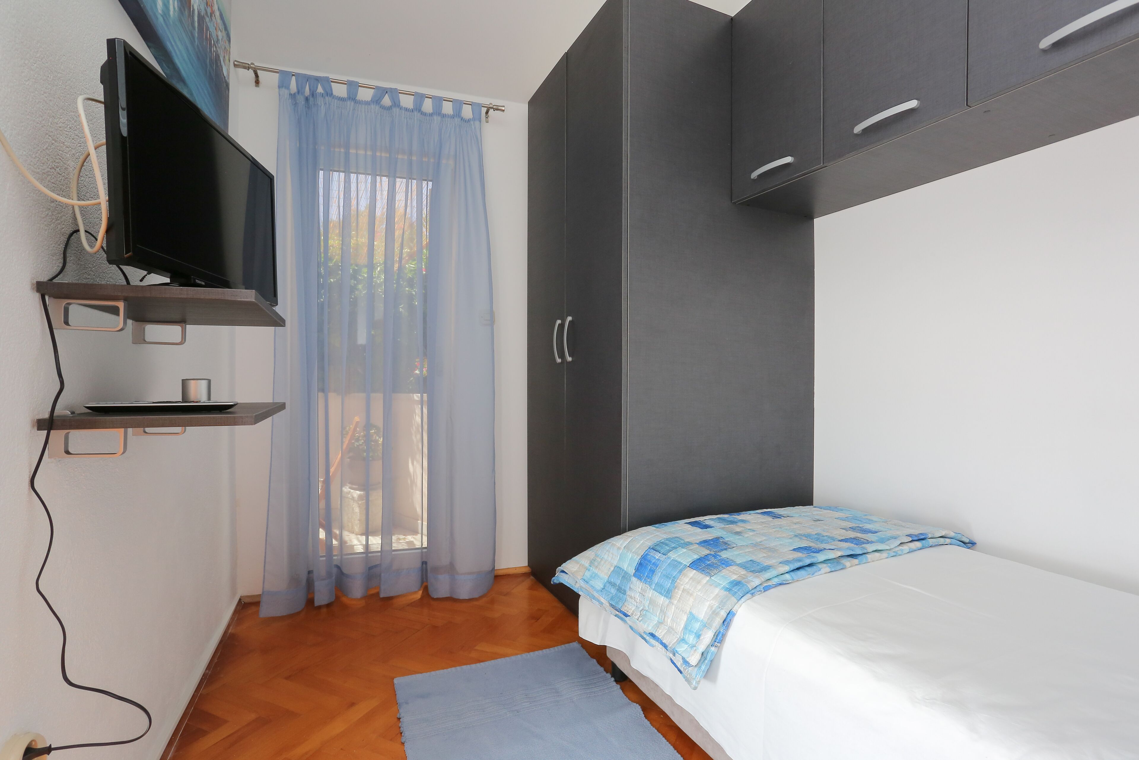 A bedroom with a bed, a TV mounted on a shelf, and a wardrobe.