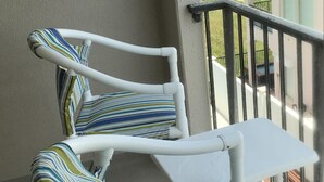 A balcony with white metal chairs and cushions, a small table, and a view of the beach and ocean. - Studio on the beach! balcony ocean view, sleeps 4. pool, hot tub, BBQ. (South Padre Island)