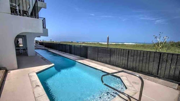 A swimming pool with a view of the ocean, a fenced area, and a building with a balcony. - Studio on the beach! balcony ocean view, sleeps 4. pool, hot tub, BBQ. (South Padre Island)