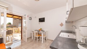 A compact kitchen with a dining area, a TV mounted on the wall, and a view of the outside balcony. - Apartments Magdalena (Bol)