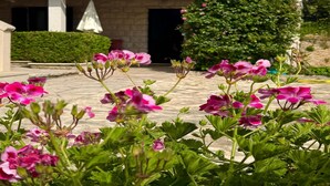 A building with a tiled roof, a stone facade, and a garden with pink flowers in the foreground. - Apartments Magdalena (Bol)