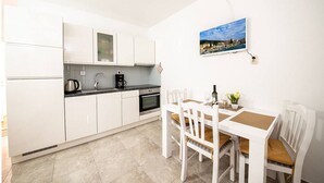 A compact kitchen with white cabinets, a black countertop, and a dining area with a white table and chairs. - Apartments Magdalena (Bol)