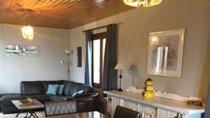 A dining area with a wooden table and leather chairs, a sofa, and a kitchen area with a white countertop and a hanging light fixture. - Le Vignal 1, quiet cottage in the south of the Ardèche (Chambonas)