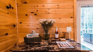 Interior de madera con un mostrador de recepción, un jarrón de flores, una cesta con un letrero y una botella de licor.