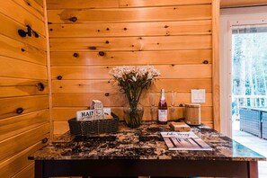 Un intérieur en bois comprenant un comptoir d’accueil, un vase de fleurs, un panier avec une pancarte et une bouteille de spiritueux.