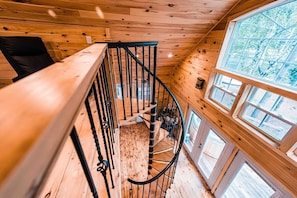 Un interior de madera con una escalera de caracol, ventanas grandes y vistas al exterior.