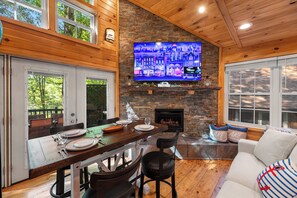 Un intérieur chaleureux avec une cheminée en pierre, un coin repas avec une table en bois dressée pour quatre personnes et un espace salon confortable avec un canapé.