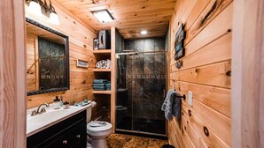 Un baño rústico en una cabaña de madera, con lavamanos, inodoro y mampara de ducha de vidrio.