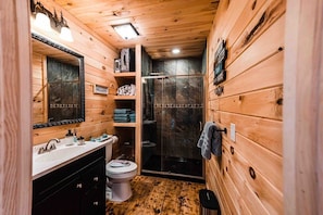Une salle de bain rustique, aménagée dans une cabane en bois, avec un lavabo, des toilettes et une douche à parois en verre.